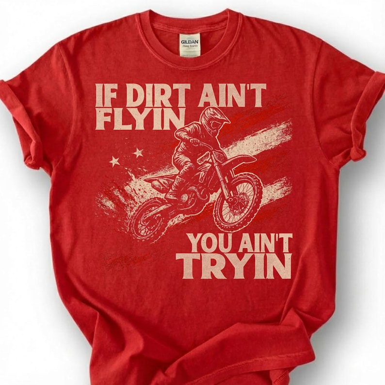 Peut inclure: T-shirt rouge avec le texte "IF DIRT AIN'T FLYIN, YOU AIN'T TRYIN" et un motard de motocross. Le design comprend un fond de style drapeau am&eacute;ricain vieilli et des &eacute;toiles.