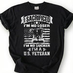 May include: Black t-shirt with a white graphic design. The design includes the word "SACRIFICED" above the text "I'M NO LOSER" and "I'M NO SUCKER I'M A U.S. VETERAN". The graphic also features combat boots and an American flag.
