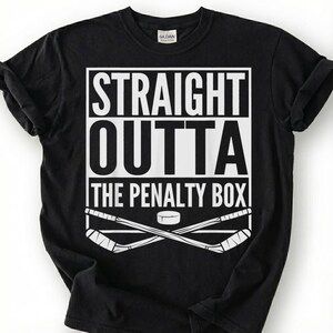 May include: Black t-shirt with a white graphic that reads "STRAIGHT OUTTA THE PENALTY BOX." The design includes crossed hockey sticks and a puck. The shirt is a Gildan brand.