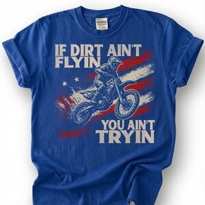 Peut inclure: T-shirt bleu avec un motif de motocross. Le design comprend un motard sur une moto, le texte "IF DIRT AIN'T FLYIN' YOU AIN'T TRYIN'" et un drapeau am&eacute;ricain rouge, blanc et bleu.