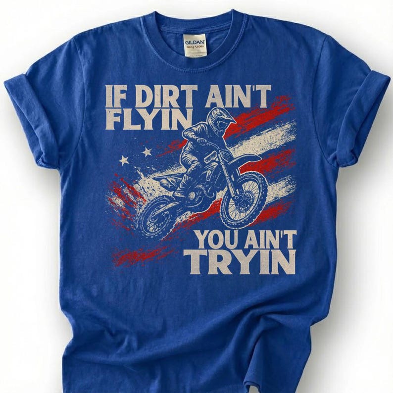 Peut inclure: T-shirt bleu avec un motif de motocross. Le design comprend un motard sur une moto, le texte "IF DIRT AIN'T FLYIN' YOU AIN'T TRYIN'" et un drapeau am&eacute;ricain rouge, blanc et bleu.