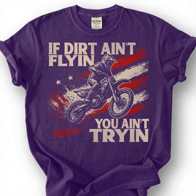 Peut inclure: T-shirt violet avec un motif de pilote de motocross et le texte "IF DIRT AIN'T FLYIN, YOU AIN'T TRYIN". Le motif int&egrave;gre le drapeau am&eacute;ricain en rouge, blanc et bleu. Le t-shirt a un col rond et des manches courtes.