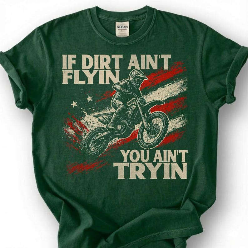 Peut inclure: T-shirt vert fonc&eacute; avec un motif d'un pilote de motocross sur une moto, sur fond de drapeau am&eacute;ricain vieilli. Le texte dit "IF DIRT AIN'T FLYIN' YOU AIN'T TRYIN'".