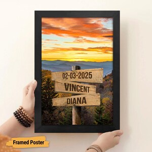 May include: Framed poster with a scenic mountain landscape at sunset. The poster features a wooden signpost with the date "02-03-2025", the names "Vincent" and "Diana", and a rustic wooden background.