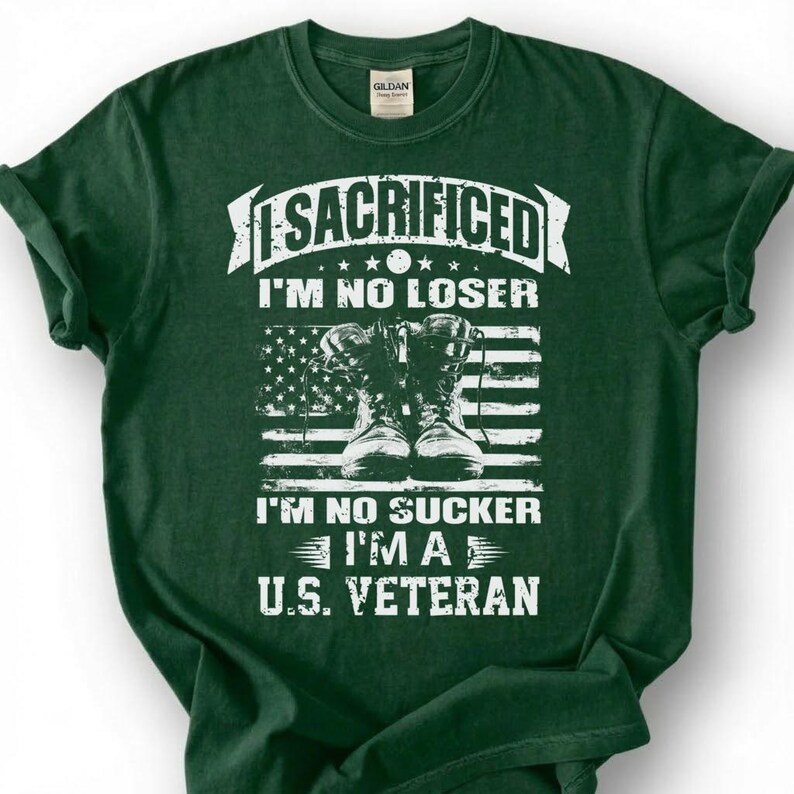 May include: Dark green t-shirt with white text and a graphic of combat boots in front of an American flag. The text reads "SACRIFICED I'M NO LOSER I'M NO SUCKER I'M A U.S. VETERAN."