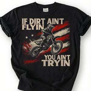 Peut inclure: T-shirt noir avec un motif d'un pilote de motocross sur une moto, sur fond de drapeau am&eacute;ricain vieilli. Le texte dit : &laquo; IF DIRT AIN'T FLYIN, YOU AIN'T TRYIN &raquo;.