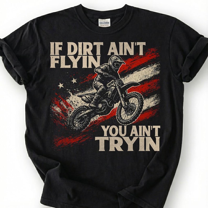 Peut inclure: T-shirt noir avec un motif d'un pilote de motocross sur une moto, sur fond de drapeau am&eacute;ricain vieilli. Le texte dit : &laquo; IF DIRT AIN'T FLYIN, YOU AIN'T TRYIN &raquo;.