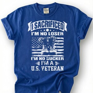 May include: Blue t-shirt with a graphic design featuring the text "SACRIFICED I'M NO LOSER I'M NO SUCKER I'M A U.S. VETERAN" and an American flag with combat boots. The shirt is made of a soft material.