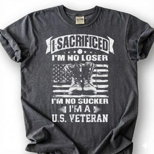 May include: Dark gray t-shirt with the text "I SACRIFICED I'M NO LOSER" above an American flag graphic and combat boots. Below the flag, the text reads "I'M NO SUCKER I'M A U.S. VETERAN". The shirt has a crew neck and short sleeves.