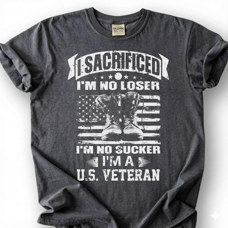 May include: Dark gray t-shirt with the text "I SACRIFICED I'M NO LOSER" above an American flag graphic and combat boots. Below the flag, the text reads "I'M NO SUCKER I'M A U.S. VETERAN". The shirt has a crew neck and short sleeves.