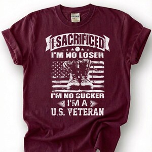 May include: Burgundy t-shirt with a graphic design. The design includes the text "I SACRIFICED I'M NO LOSER I'M NO SUCKER I'M A U.S. VETERAN" above a depiction of combat boots and an American flag.