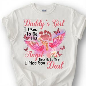 May include: White t-shirt with a graphic design featuring the text "Daddy's Girl" and "I Miss You Dad". The design includes a footprint, angel wings, butterflies, and floral accents in pink and red.