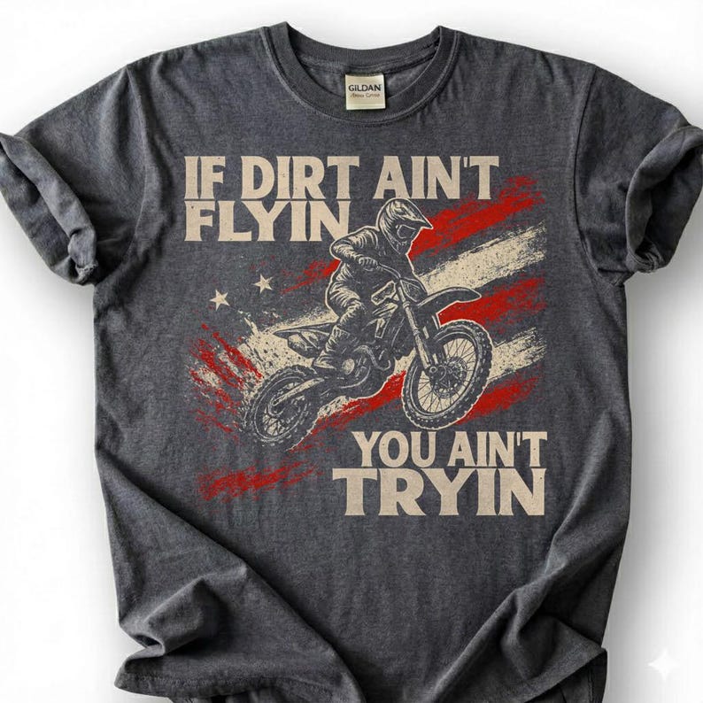 Peut inclure: T-shirt gris fonc&eacute; avec un motif de pilote de motocross sur une moto tout-terrain. Le design comprend un motif de drapeau am&eacute;ricain et le texte "IF DIRT AIN'T FLYIN YOU AIN'T TRYIN".