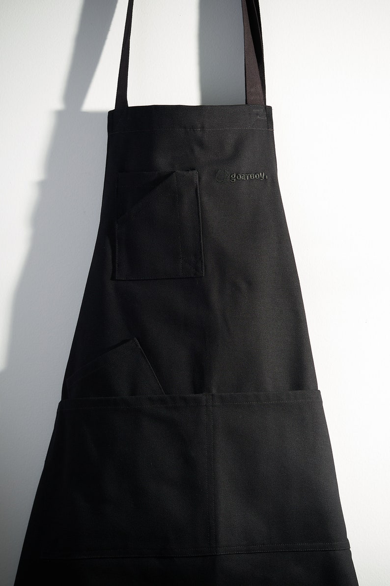 May include: Black apron with two pockets and adjustable straps. The apron has the word "goatboy" embroidered on the front.