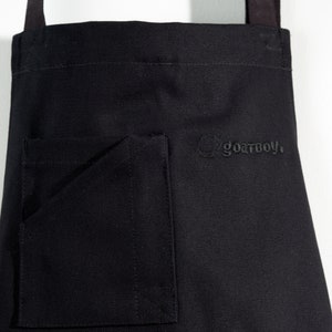 May include: Black canvas apron with a large pocket and the text "goatboy." embroidered on the front.