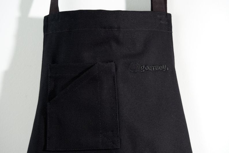 May include: Black canvas apron with a large pocket and the text "goatboy." embroidered on the front.