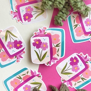 May include: Floral stickers with a rectangular design, teal border, and purple ribbon. The stickers display pink and purple flowers with green leaves. The background is white and pink.