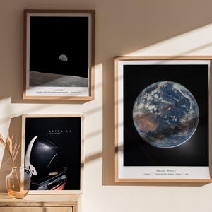 May include: Three framed art prints featuring space-themed imagery. One shows the Earth, another depicts the moon from the lunar surface, and the third displays an astronaut's helmet. The prints are in wooden frames and are displayed on a wall.