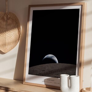 May include: A framed print featuring a view of Earth from space, with the planet's blue and white surface visible against a black background. The print is in a light wood frame and includes the text "Earthset" at the bottom.