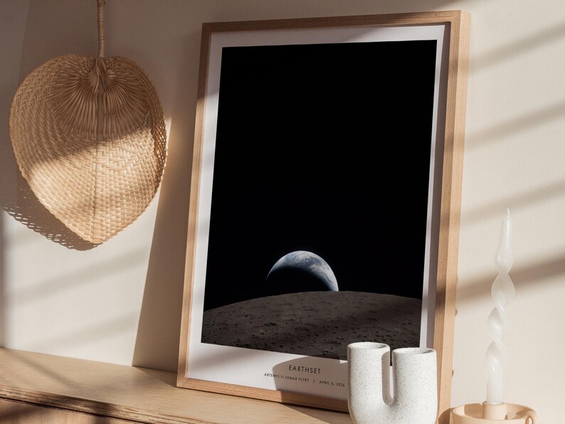 May include: A framed print featuring a view of Earth from space, with the planet's blue and white surface visible against a black background. The print is in a light wood frame and includes the text "Earthset" at the bottom.