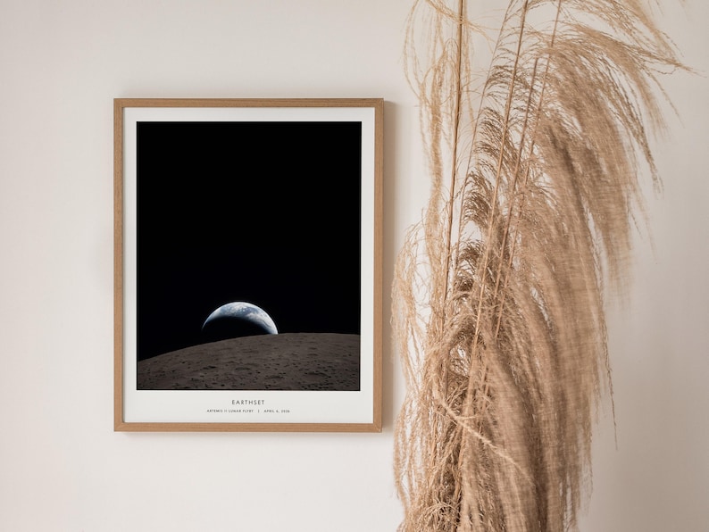 May include: A framed print of the Earth rising over the lunar surface, a classic image from the Apollo 8 mission. The print features a black sky, a gray lunar surface, and the Earth in shades of blue and white. The print is in a wooden frame.