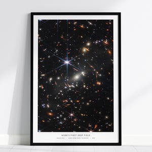 May include: Framed print of the James Webb Space Telescope's First Deep Field image, showcasing a dense field of galaxies and stars against a dark background. The image is in a black frame and includes the text "WEBB'S FIRST DEEP FIELD".