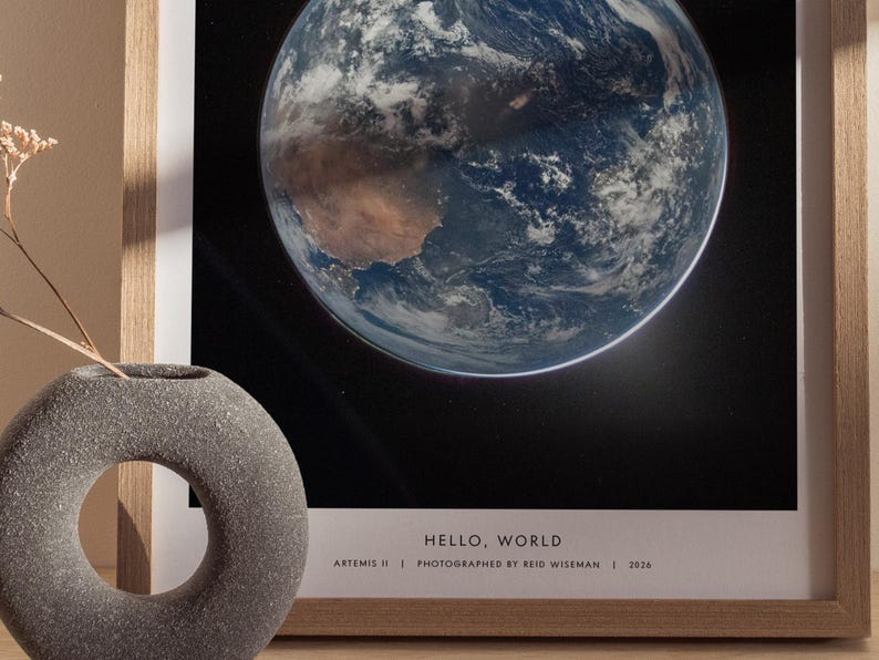 May include: Framed print of Earth from space, showcasing blue oceans, brown continents, and white clouds against a black background. The print is in a light wood frame. Text at the bottom reads "HELLO, WORLD" and details about the photograph.