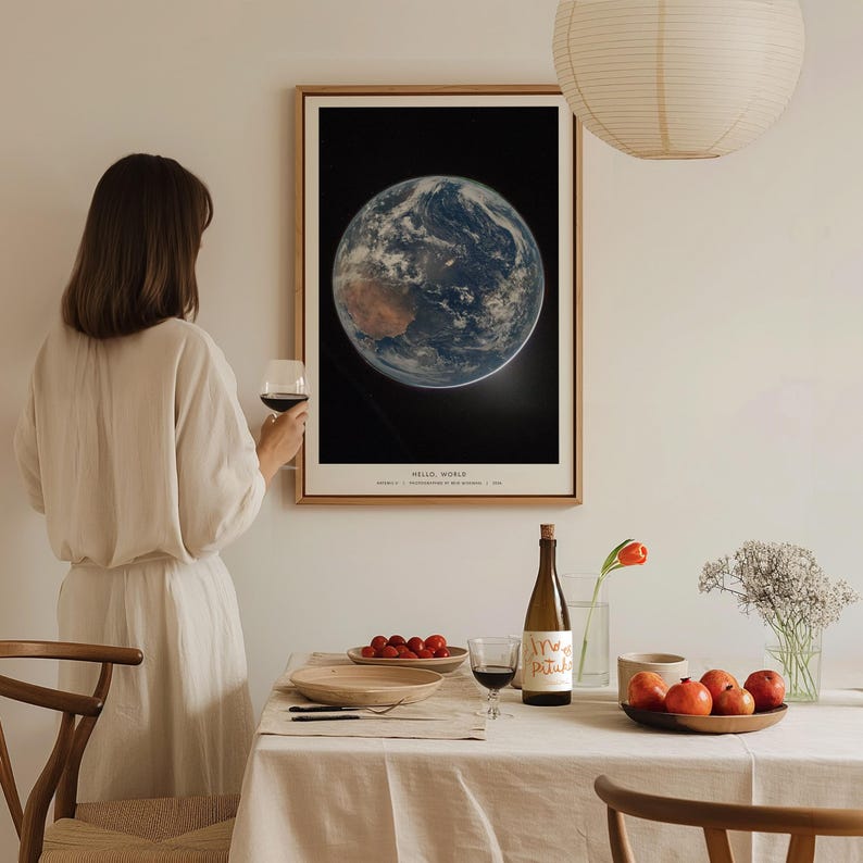 May include: A framed print of Earth from space, with continents and clouds visible against a black background. The print is in a wooden frame and hangs on a white wall. The text "HELLO, WORLD" is at the bottom of the print.