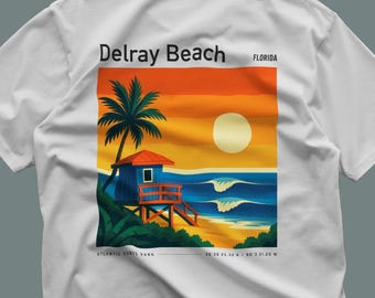 Puede incluir: Camiseta blanca con un diseño de playa vibrante. El diseño incluye un puesto de salvavidas, una palmera y olas del océano bajo un cielo al atardecer. El texto en la camiseta dice "Delray Beach Florida" y "Atlantic Dunes Park".