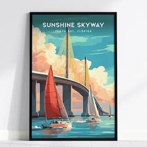 May include: A framed art print featuring the Sunshine Skyway Bridge in Tampa Bay, Florida. The artwork depicts sailboats on the water with the bridge in the background. The sky is a mix of blue and orange hues, and the print is in a black frame.