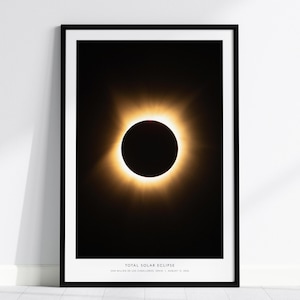 Könnte beinhalten: Ein gerahmter Wandkunstdruck, der eine totale Sonnenfinsternis mit einem dunklen zentralen Mond zeigt, umgeben von einer hellen goldenen Korona. Am unteren Rand des Drucks steht der Text TOTAL SOLAR ECLIPSE, SAN MILLAN DE LOS CABALLEROS, SPAIN, AUGUST 12, 2026.