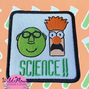 May include: A square embroidered patch with a light blue background and a black border. It features a green circular character wearing glasses next to an orange-haired character with a wide-eyed expression. The word SCIENCE!! is stitched in green.