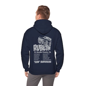 May include: A navy blue hooded sweatshirt with a white graphic of a Jeep Rubicon driving off-road. The graphic includes the text "Rubicon", "El Dorado County, CA", and a list of trails. The text "CON" SURVIVOR" is also included in the graphic.