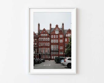 May include: A red brick building with multiple windows and a row of cars parked in front.