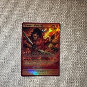 May include: A holographic trading card featuring "Oden & Infernape" with a red and orange color scheme. The card displays two characters, one wielding a sword, and the other with flames. The card has text describing abilities and damage.