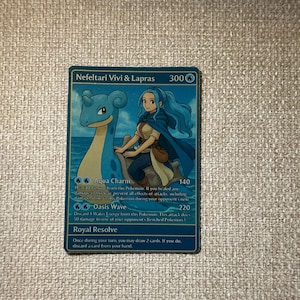 May include: A blue trading card featuring Nefeltari Vivi & Lapras. The card depicts a blue Lapras and a woman with blue hair. The card has the text "Aqua Charm", "Oasis Wave", and "Royal Resolve".