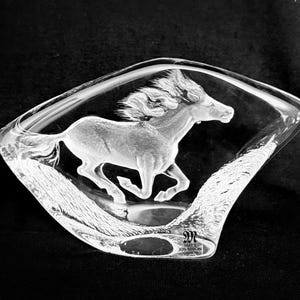 May include: A clear glass sculpture of a running horse, etched within a diamond-shaped frame. The horse is depicted with flowing mane and tail, set against a textured background. The base of the sculpture has the artist's signature.