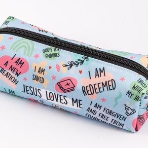May include: A light blue pencil case with a zipper closure. The case is decorated with a colourful pattern of hearts, stars, rainbows, and text that reads "I am a new creation", "I am saved", "Jesus loves me", "I am redeemed", "I am forgiven and free from condemnation", "God's love endures", "Trust God with all your heart", and "I will give God glory".