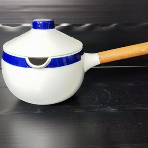 Puede incluir: Salsera de cerámica blanca con una franja azul y un asa de madera. La tapa tiene un pequeño pico.