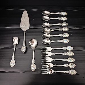Peut inclure: Un ensemble d'argenterie ancienne, comprenant des cuillères, des fourchettes et des ustensiles de service, disposés sur une surface noire. L'argenterie présente des motifs floraux ornés sur les manches. L'ensemble comprend une pelle à gâteau et une cuillère à sucre.