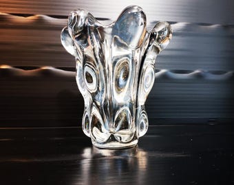 May include: A clear glass vase featuring a thick, heavy base and a series of vertical, rounded indentations that create a rippled, organic texture along the exterior. The rim is uneven and undulating, following the contours of the glass body.