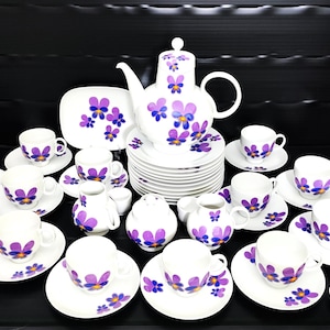 May include: A complete white porcelain tea set with purple floral designs. The set includes a teapot, cups, saucers, serving dishes, and a sugar bowl. The floral pattern features purple and blue flowers.
