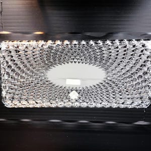 May include: A rectangular, clear glass tissue box with a textured, diamond-like pattern. The top features an oval opening for tissue dispensing. The box is made of a transparent material, allowing visibility of the contents.