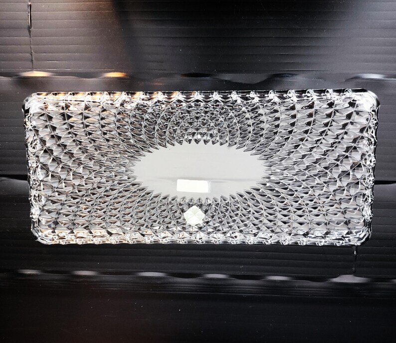 May include: A rectangular, clear glass tissue box with a textured, diamond-like pattern. The top features an oval opening for tissue dispensing. The box is made of a transparent material, allowing visibility of the contents.