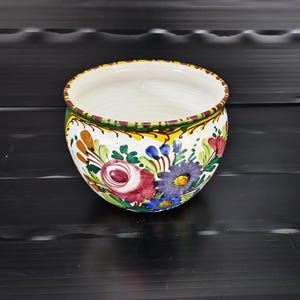 Könnte beinhalten: Eine weiße Keramik-Tasse mit schwarzem Henkel und dem Text "But First, Coffee" in fetter, schwarzer Schrift. Die Tasse steht vor einem verschwommenen Hintergrund, der eine gemütliche Umgebung suggeriert.