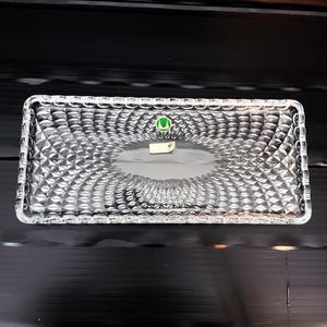 May include: A rectangular clear glass tray with a diamond pattern. The tray has a slightly raised edge and a smooth, oval-shaped center. A small green and white sticker is visible on the tray's surface.