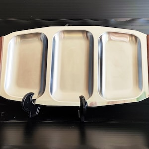 Op de afbeelding: Een zilveren dienblad met drie rechthoekige compartimenten, elk met een glad, gepolijst oppervlak. Het dienblad heeft een houten frame met een donkerbruine afwerking.