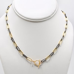 May include: A gold and black chain necklace with a toggle clasp. The chain is made of linked oval shapes.