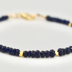 Pode incluir: Um delicado bracelete feito com pequenas contas de lapis-lazúli facetadas e detalhes dourados.
