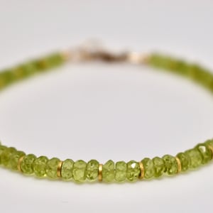 May include: A green peridot gemstone bracelet with gold beads. The bracelet is made of small, faceted peridot beads and gold beads.